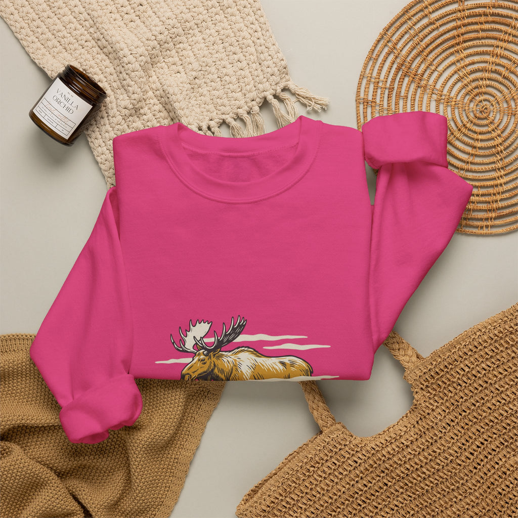 Heliconia North Woods Moose Crewneck laid flat next to a woven basket and knit blanket