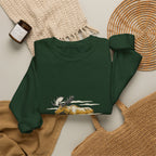 Forest Green North Woods Moose Crewneck laid flat next to a woven basket and knit blanket